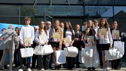 Na zdjęciu grupa młodzieży ubrana w eleganckie stroje z dyplomami w rękach