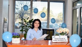 Powiększ obraz:Pracownik starostwa, ma niebieską bluzkę, stoi za ladą, w tle niebieskie baloniki