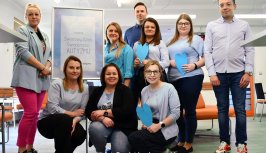 Powiększ obraz:Grupa praconików starostwa, którzy mają założone niebieskie elementy garderoby, stoją w holu, w tle niebieskie serduszka i tablica
