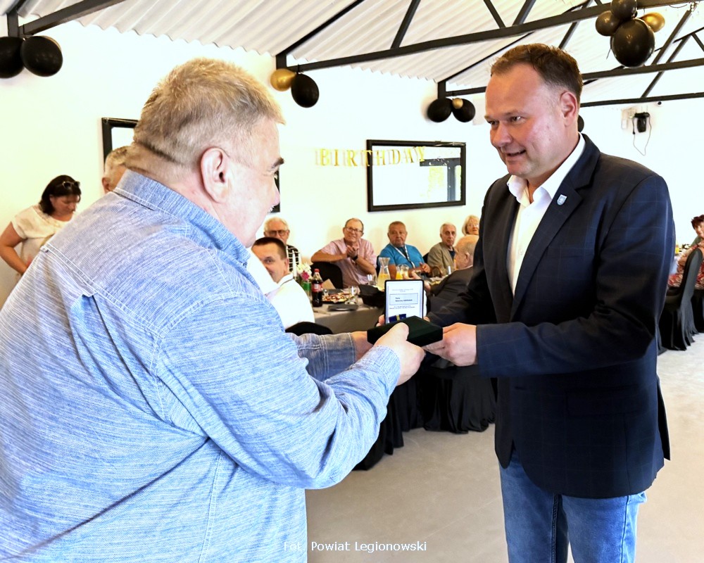 Na zdjęciu widać dwóch mężczyzn, jeden drugiemu wręcza odznaczenie