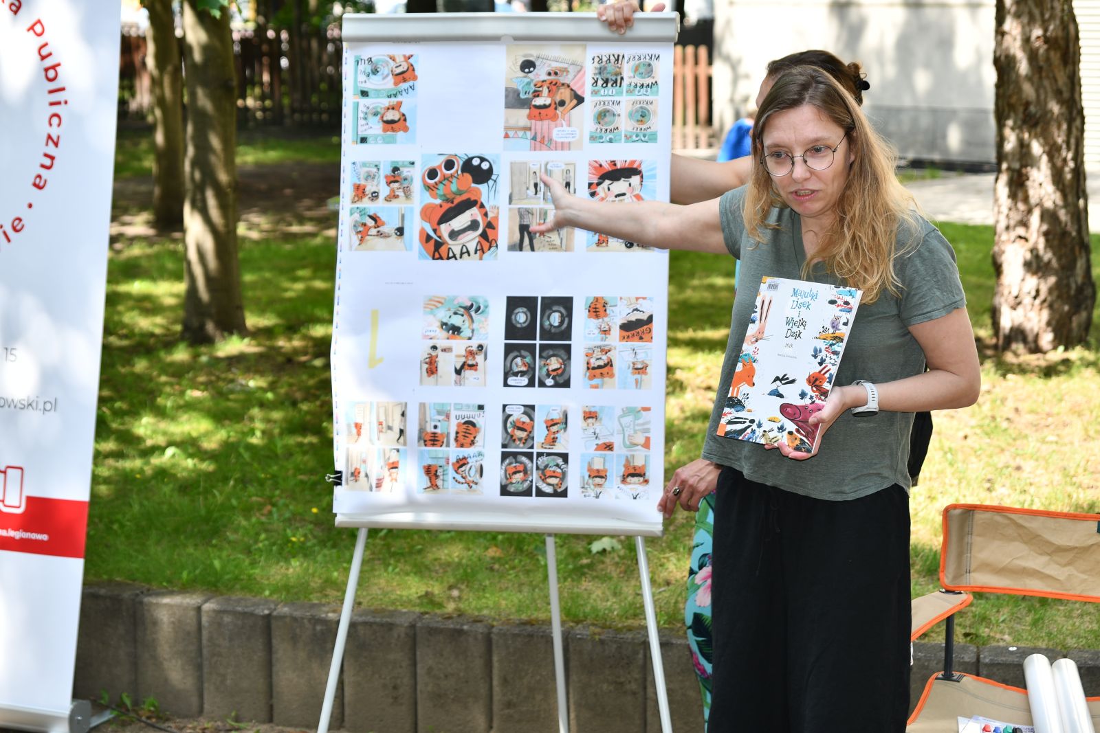 Na zdjęciu autorka książki kobieta w zielonej bluzce w okularach pokazuje tablicę z rysunkami